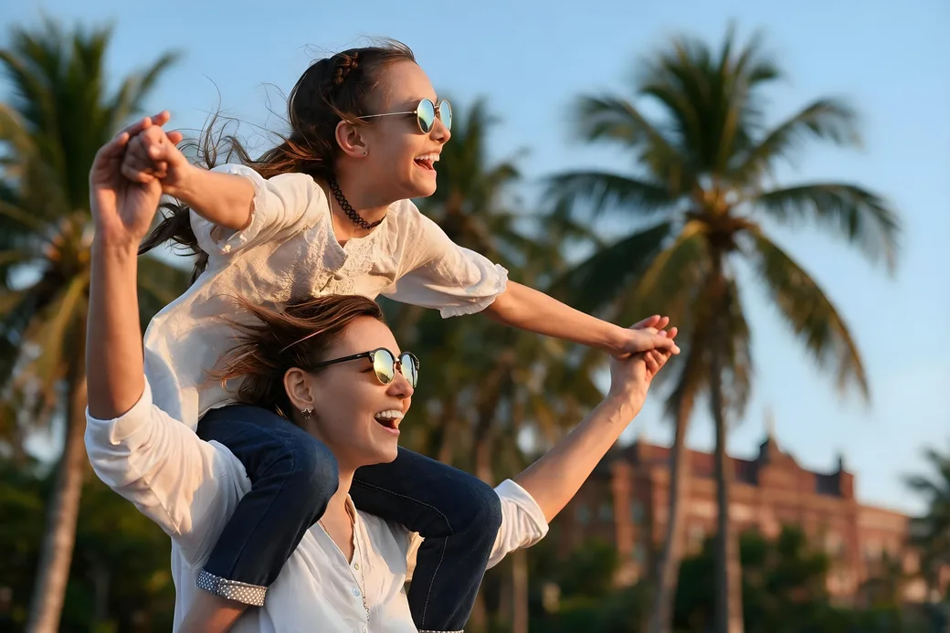 A child on a parent&rsquo;s shoulders under palm trees